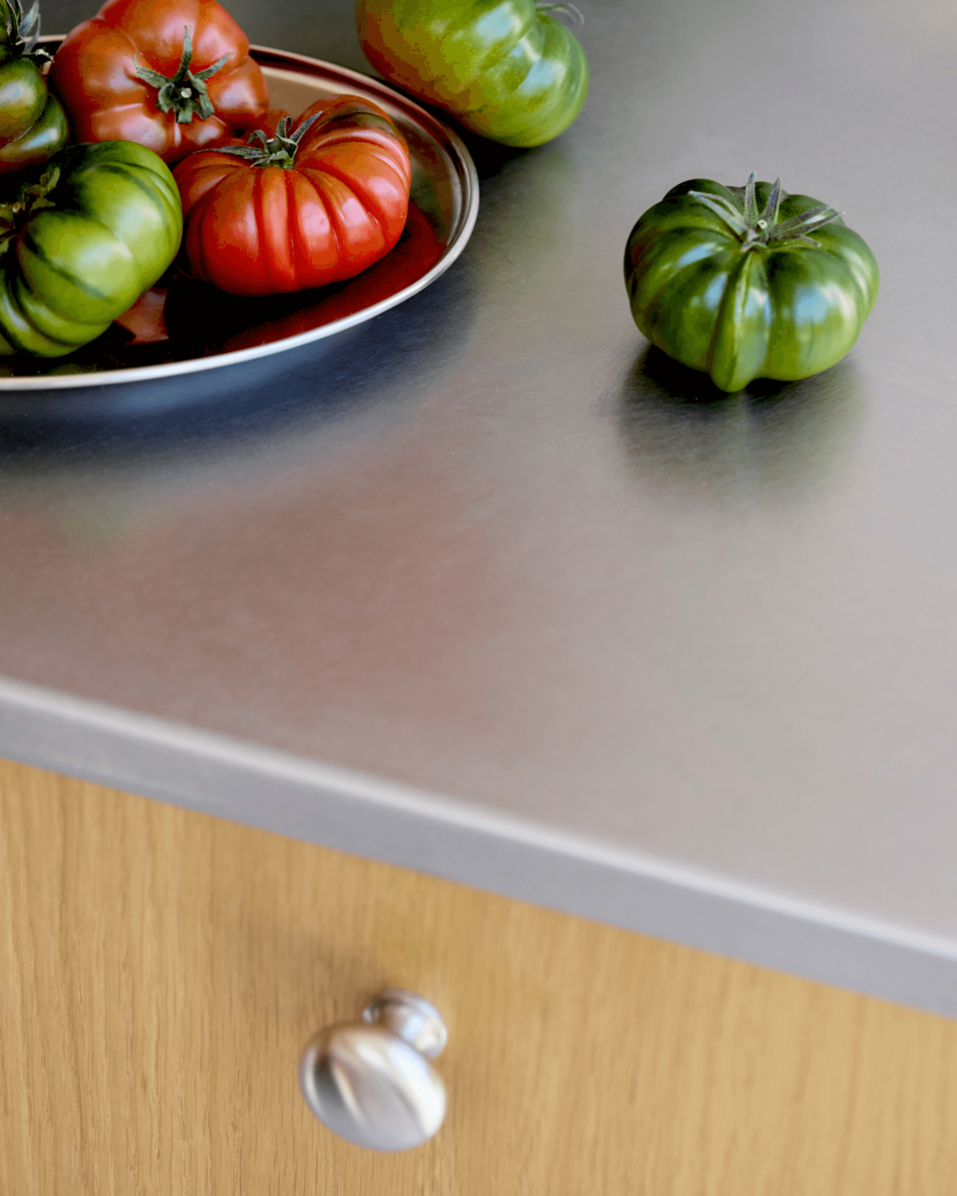 Stainless steel worktop topped with red and green tomatoes.