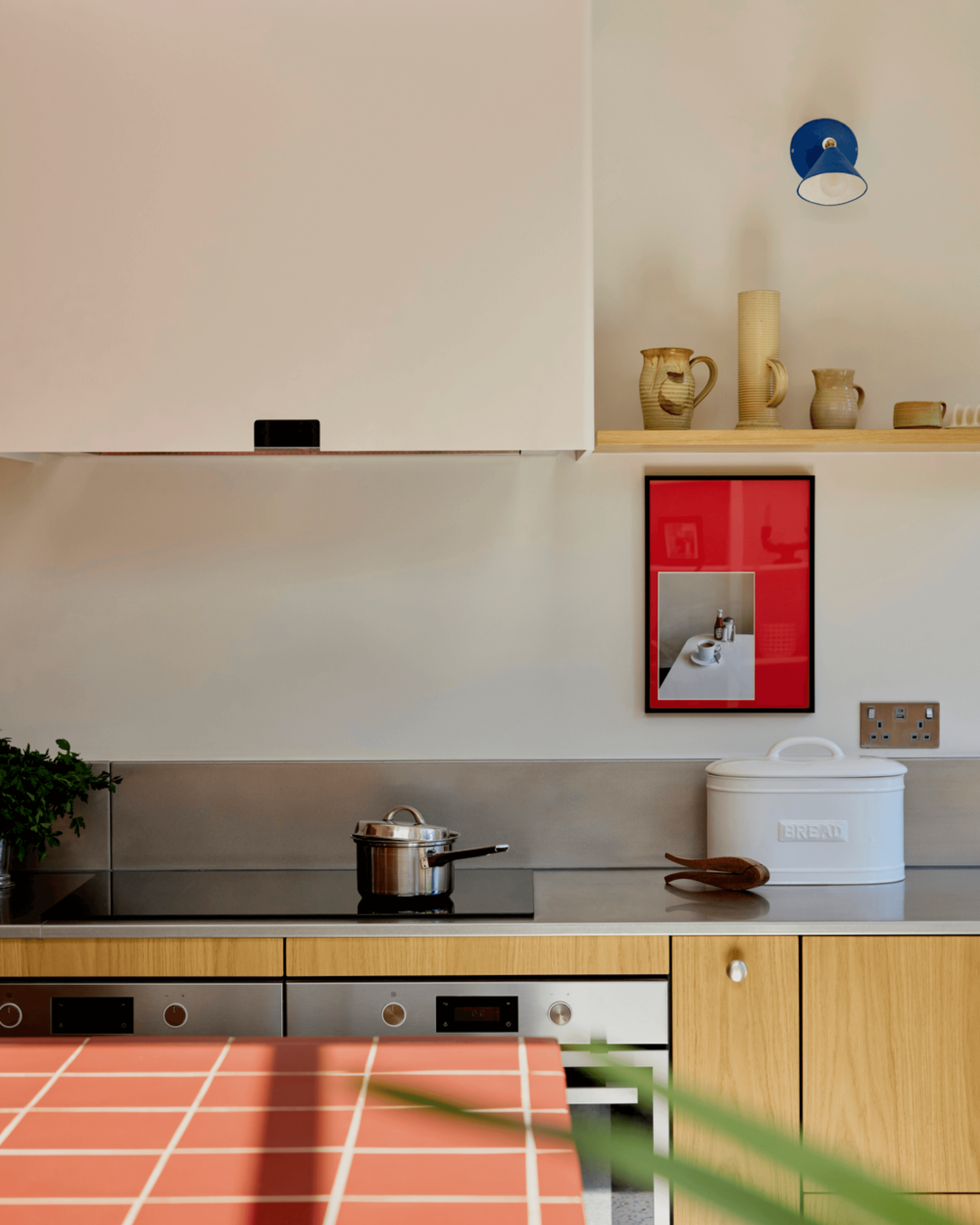 Oak veneer fronts and stainless steel worktop in a vibrant modern kitchen, featuring saucepan and bread bin.