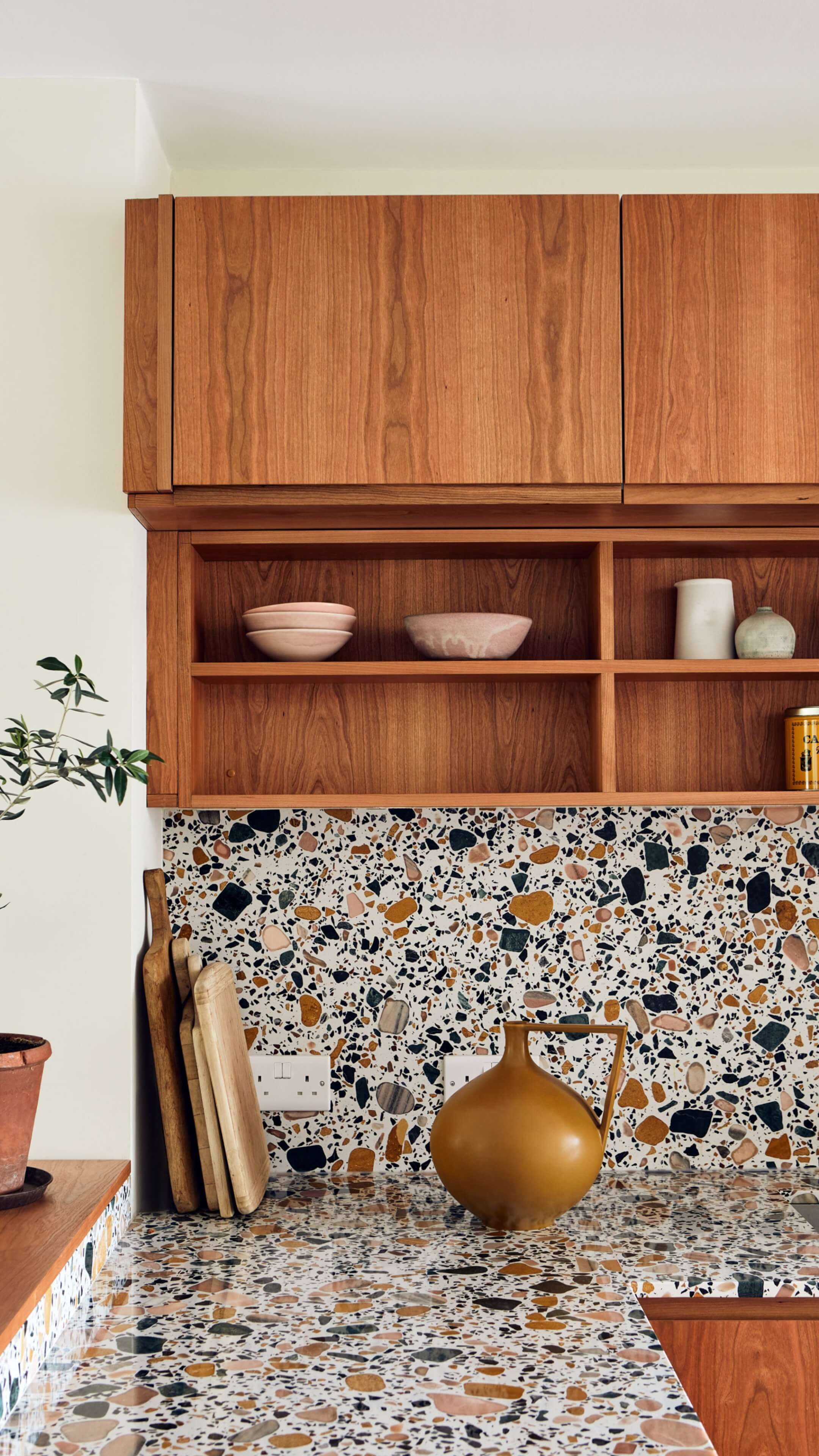 Close up photo of terrazzo worktop and backsplash in kitchen with wooden shelving and cabinet doors